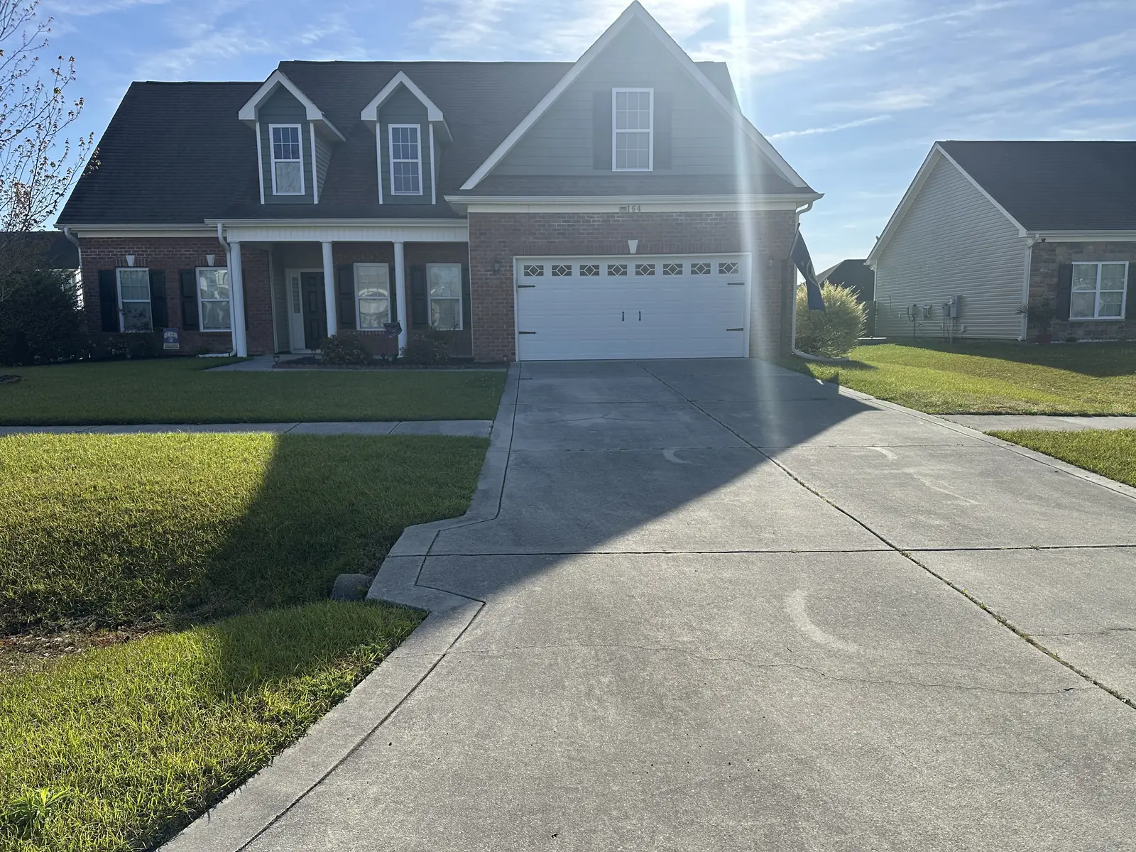 Before: brick and vinyl two-story house with stained concrete driveway before washing