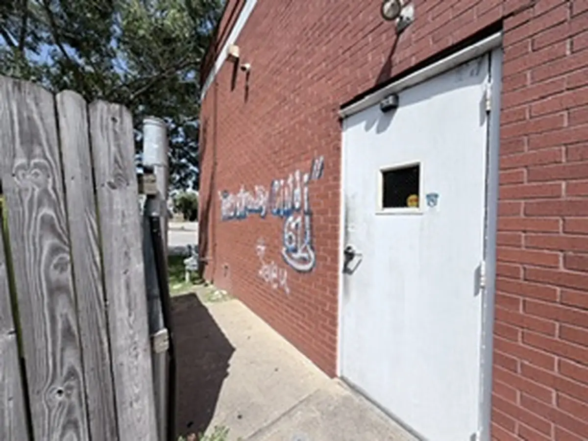 Before: spray-painted graffiti tag on the red brick wall beside a commercial building's service door in New Bern, NC