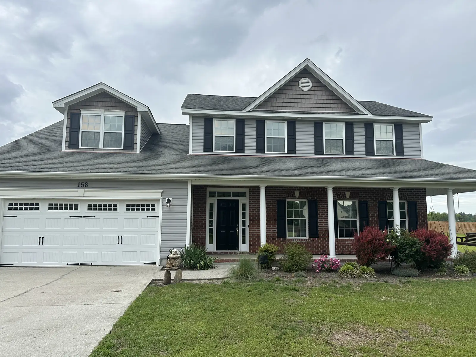 Before: two-story gray vinyl house with brick accent and covered porch with algae and weathering on siding