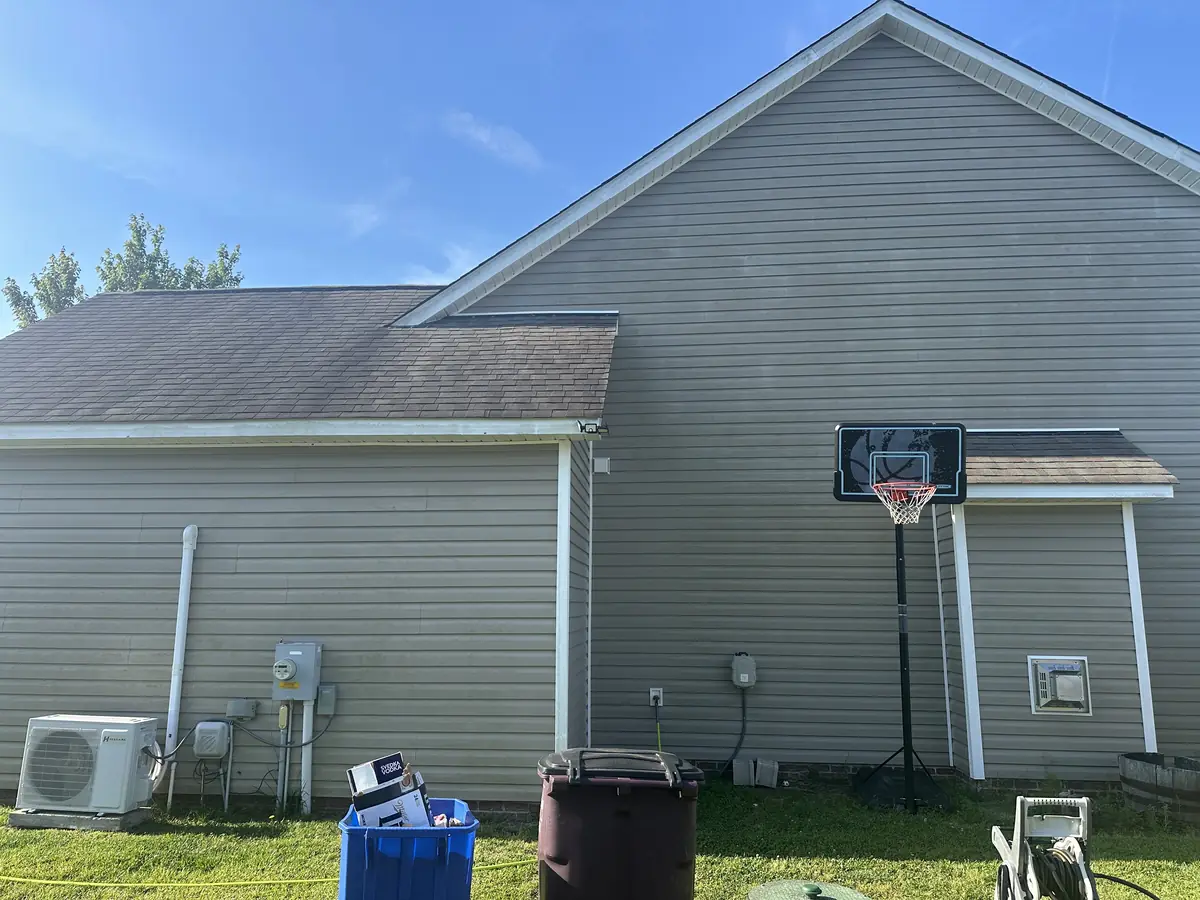 Before: side of gray vinyl home with algae on siding next to basketball hoop before soft wash