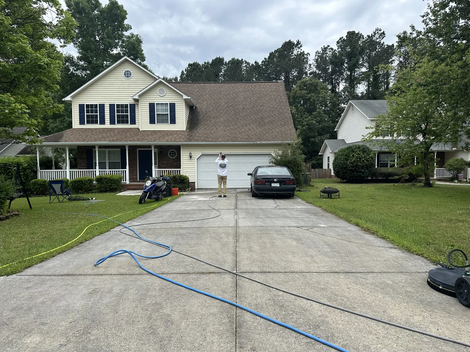 Before: two-story yellow house with stained concrete driveway before pressure washing